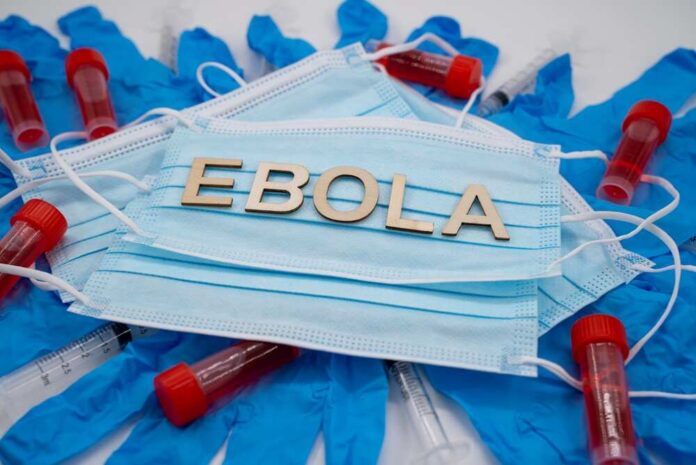 Ebola,Medical,Concept,With,Masks,Gloves,And,Laboratory,Samples. Ebola test tubes on lab table with gloved scientist in background