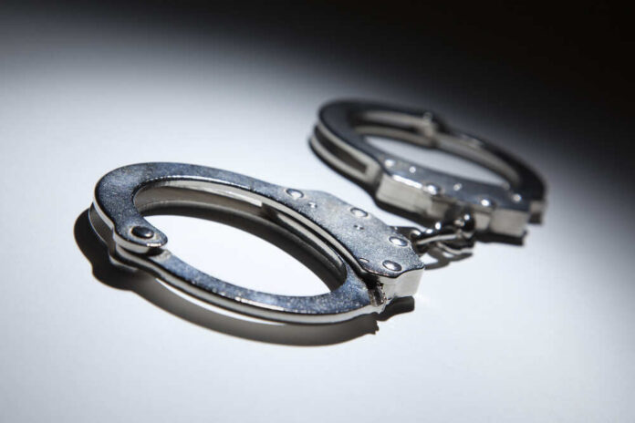 Abstract,Pair,Of,Handcuffs,Under,Spot,Light,On,Gradated,Background. Close-up of metallic handcuffs on a light surface