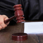 Parents Demand Death For Singer Judges hand holding gavel next to documents.