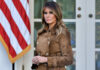 Melania Crashes Wall Street – Announces THIS! Melania Trump standing outdoors in a brown suede trench coat