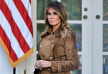 Melania Trump standing outdoors in a brown suede trench coat