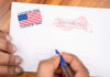 Election Twist: Trump Admin Says It Will Comply Hands addressing an official election mail envelope
