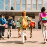 Group of schoolchildren with backpacks running toward a school entrance