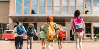Group of schoolchildren with backpacks running toward a school entrance