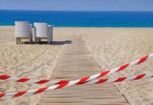 A wooden pathway leading to the beach with restricted access tape and chairs in the background