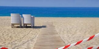 A wooden pathway leading to the beach with restricted access tape and chairs in the background