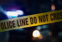 Midnight Hit Kills Sports Club Boss Police tape with blurred emergency lights in the background