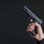 Hand holding a black semi-automatic pistol against a dark background