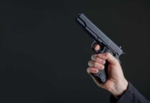 Warning Signs Ignored — Then Deadly Gunfire Hand holding a black semi-automatic pistol against a dark background