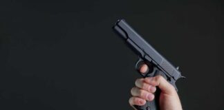 Hand holding a black semi-automatic pistol against a dark background