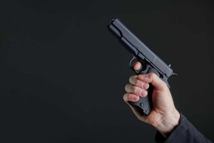 Male,Hand,Holding,A,Gun,On,Black,Background,.,A Hand holding a black semi-automatic pistol against a dark background