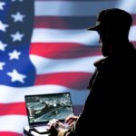 Silhouette of a person using a laptop before a large US flag