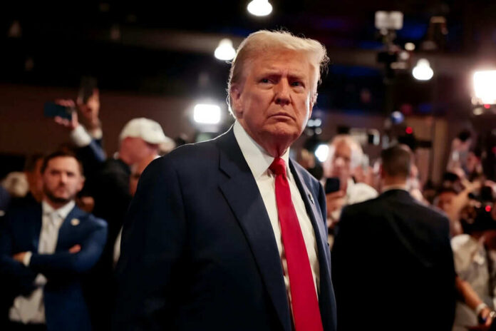 shutterstock_2549626775 Donald Trump in a navy suit with red tie at an event with cameras and crowd