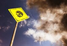Yellow warning sign with skull symbol under dramatic cloudy sky