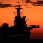 Aircraft carrier silhouette with jets at sunset