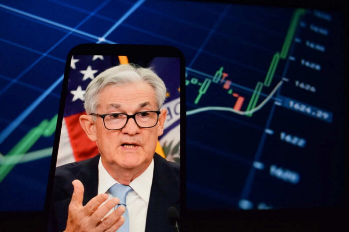 Jerome Powell speaking on a smartphone screen with stock chart in background