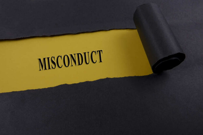 Torn,Black,Paper,On,Yellow,Surface,With,"misconduct",Word.,Business Torn black paper revealing the word 'MISCONDUCT' on yellow paper