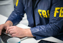 More FBI Turmoil Revealed This Week Person in FBI jacket working on laptop.