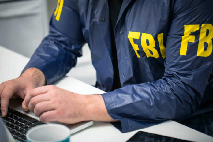 shutterstock_629482379 Person in FBI jacket working on laptop.