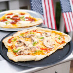 Homemade pizzas on grill trays with vegetable and pepperoni toppings