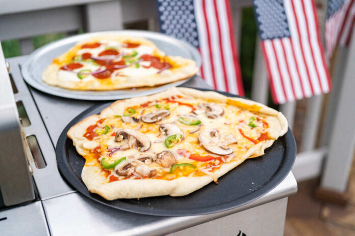 Preparing,Individual,Grilled,Pizzas,On,An,Outdoor,Gas,Grill. Homemade pizzas on grill trays with vegetable and pepperoni toppings