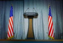 Loyalist Takes the Mic – Buckle Up Podium between two American flags on a stage