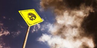 Yellow warning sign with skull symbol under dramatic cloudy sky