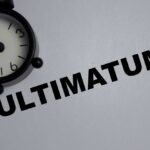 A black alarm clock next to the word 'ULTIMATUM' on a gray background