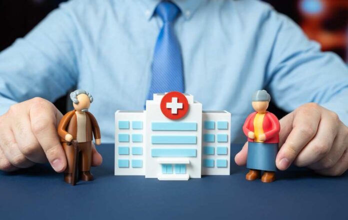 Hands holding senior figurines beside a toy hospital building